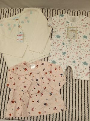 trois vêtements de bébé disposés sur une couverture posée sur un lit