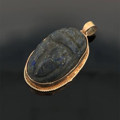 un gros plan d'un pendentif en pierre dorée et bleue sur un fond noir