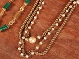 several different necklaces with pearls and gold chains on a wooden surface