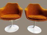 une paire de chaises pivotantes orange avec des pieds blancs sur fond gris