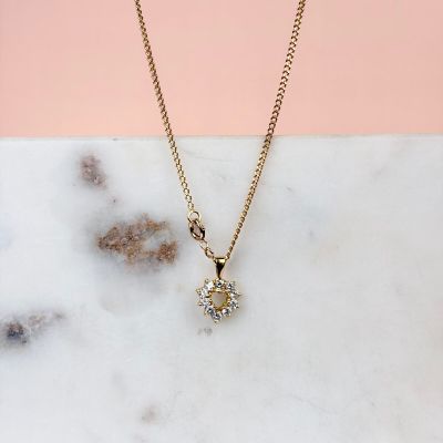 un collier en or orné d'un pendentif en forme de fleur sertie d'un diamant, posé sur une surface en marbre