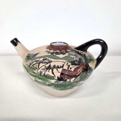 a teapot with a painting on it sitting on a table
