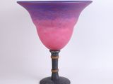 pink and purple glass vase on black stand against a white background