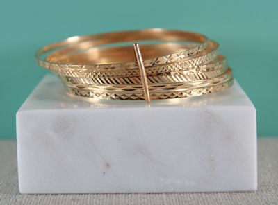 un gros plan sur une pile de bracelets en or posés sur un bloc de marbre