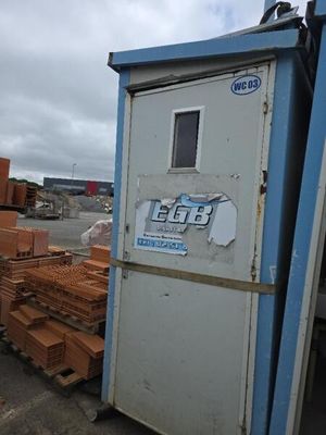 une boîte bleue et blanche sur laquelle est apposée une pancarte, à côté d'un tas de briques
