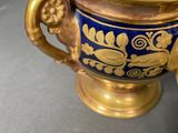 a blue and gold vase sitting on a table next to a cup