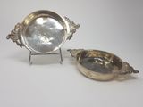 two silver plate dishes on stands on a white surface