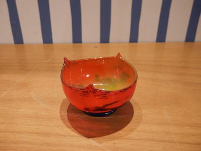 un bol rouge posé sur une table en bois, avec en arrière-plan un mur rayé de bleu et de blanc