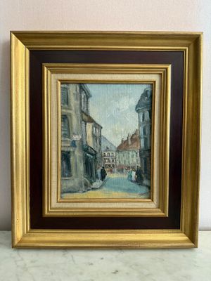 une peinture à l'huile représentant une scène de rue, dans un cadre doré, posée sur une surface en marbre