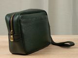 green leather cross body bag on wooden table with curtain in background