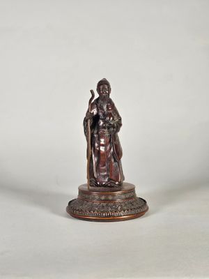 une statue en bronze représentant un homme tenant un bâton, posée sur un socle
