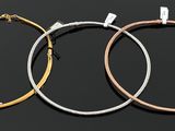 three different colored metal hoop earrings on a black background