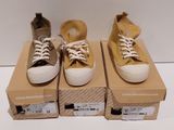 trois paires de chaussures sont posées sur des cartons, sur une surface blanche