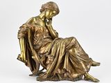 une statue en bronze représentant une femme assise sur une chaise, la main posée sur le menton