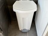 a white trash can next to a refrigerator in a bathroom