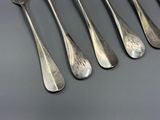 six cuillères en argent et une fourchette sont alignées sur une table