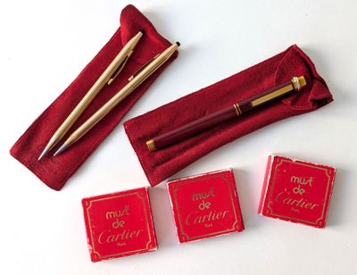 trois boîtes rouges ornées d'une inscription dorée et un stylo dans un étui rouge