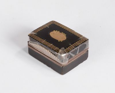 une petite boîte noire et dorée posée sur une surface blanche