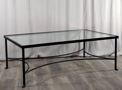 La table en verre est posée sur un parquet, devant un rideau blanc