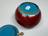 a red vase with a blue lid sitting on a table