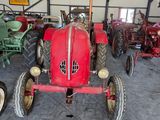 a red tractor sitting in a garage with other antique tractors