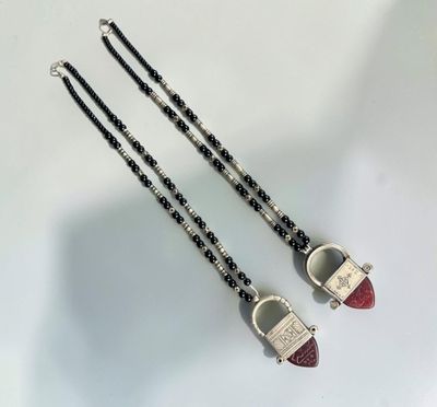 deux colliers noirs et blancs ornés de perles rouges sur un fond blanc