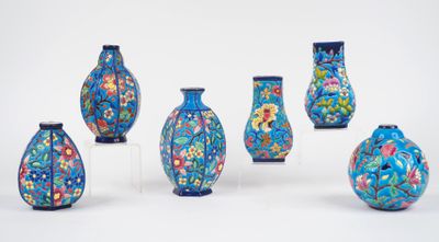 six vases bleus ornés de motifs floraux sont alignés sur une surface blanche