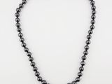 a black pearl necklace with a gold clasp on a white background