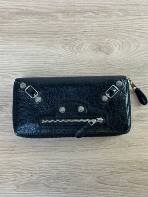 porte-monnaie en cuir noir avec des fermetures à glissière, posé sur une surface en bois