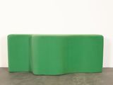a green bench sitting on top of a cement floor next to a white wall