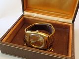 une montre en or dans un coffret marron posée sur une surface blanche
