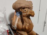 une statue représentant un chameau assis sur une table, à côté d'un récipient en plastique