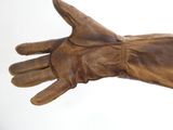 Quelqu'un tient une paire de gants en cuir marron posés sur une surface blanche.