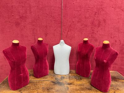 three mannequins and a bottle on a table in front of a red wall