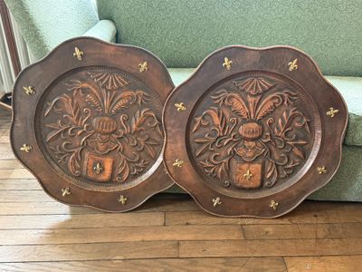 une paire d'assiettes anciennes en bois sculpté posées sur un parquet, à côté d'un canapé vert
