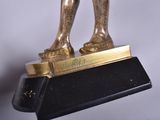 a gold statue of a man holding a tennis racquet on a black base