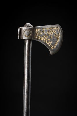 a close up of a silver and gold axe on a black background