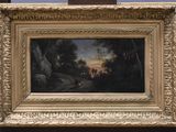 une peinture à l'huile représentant un paysage, dans un cadre doré, posée sur une table en bois