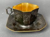 a black and gold cup and saucer on a plate