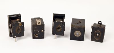 five old cameras are lined up in a row on a white surface