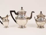 three pieces of silver tea and coffee set on a white surface