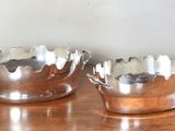 une paire de bols plaqués argent posés sur une table en bois, avec un mur blanc en arrière-plan