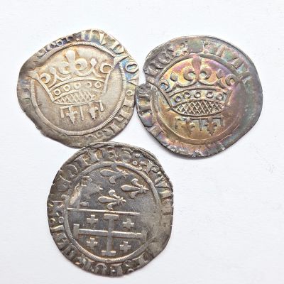 trois pièces d'argent surmontées d'une couronne, posées sur un fond blanc