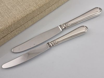 trois couteaux plaqués argent posés sur une surface blanche, à côté d'un sac en burlock