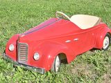 a red toy car sitting in the grass on the ground