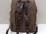 leather and canvas backpack on white surface with white wall in background