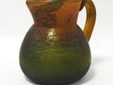 un vase marron et vert muni d'une anse, posé sur une surface blanche