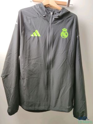 une veste grise suspendue à un cintre, sur lequel figure un logo vert