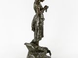 a bronze statue of a woman holding a bird on a rock