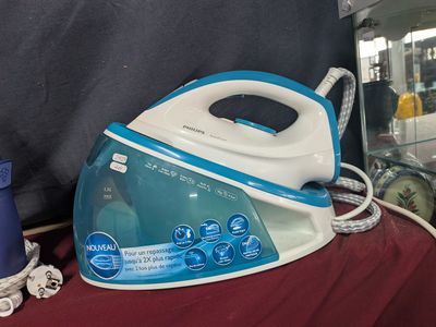 un fer à repasser à vapeur bleu et blanc posé sur un tissu rouge
